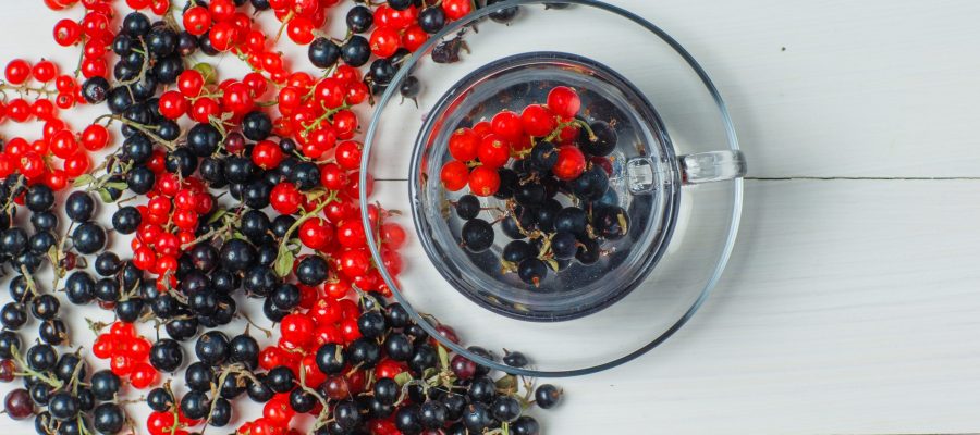 Scattered currant berries with drink on wooden background, flat lay.